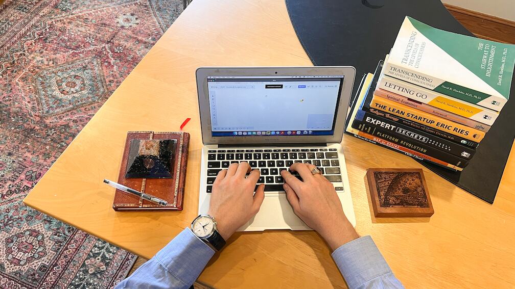Clifton Smith writing at a desk with a laptop and a stack of books