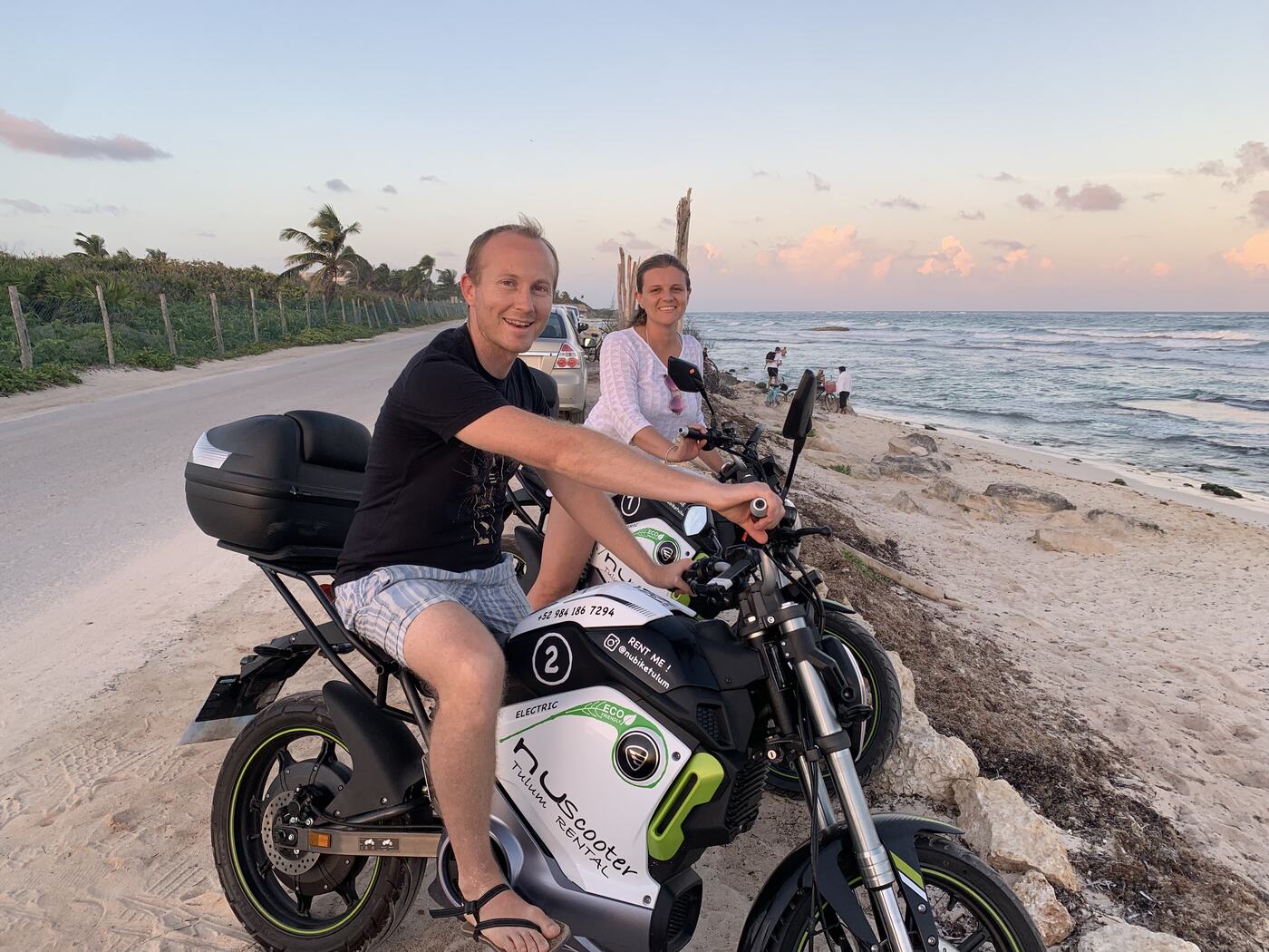 Clifton and Victoria on a motorbike on a beach road at sunset